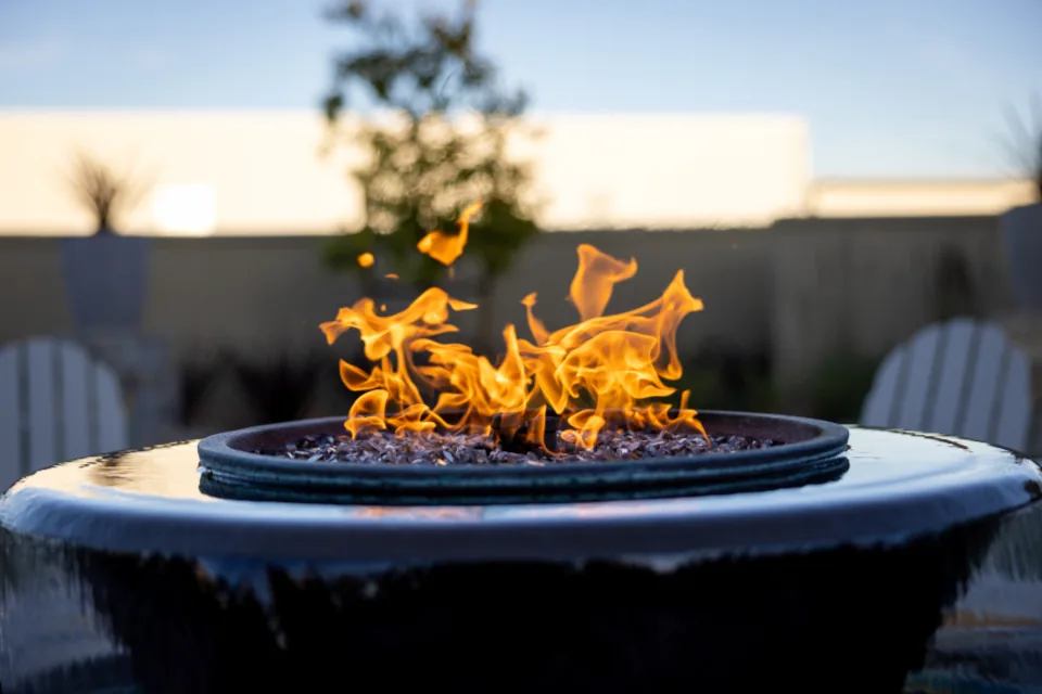 Fire bowl burning on a deck at dusk with chairs behind