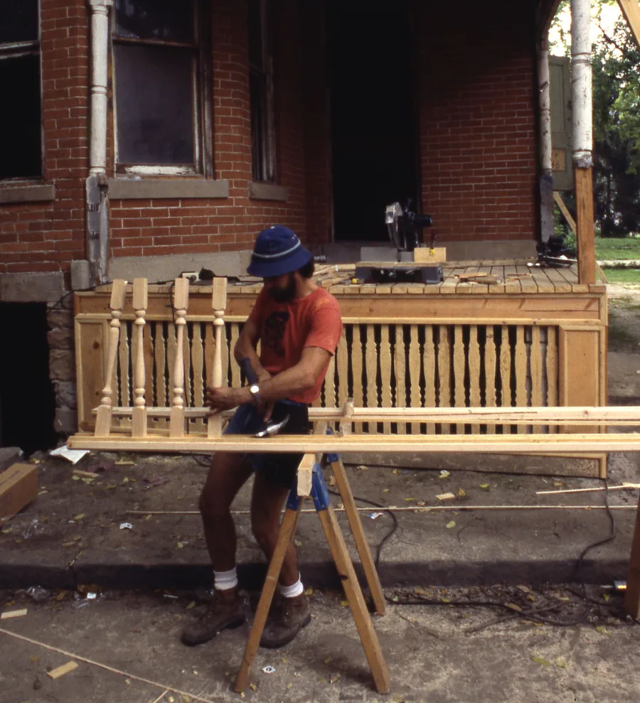 Carpenter assembling a wooden porch railing section on sawhorses