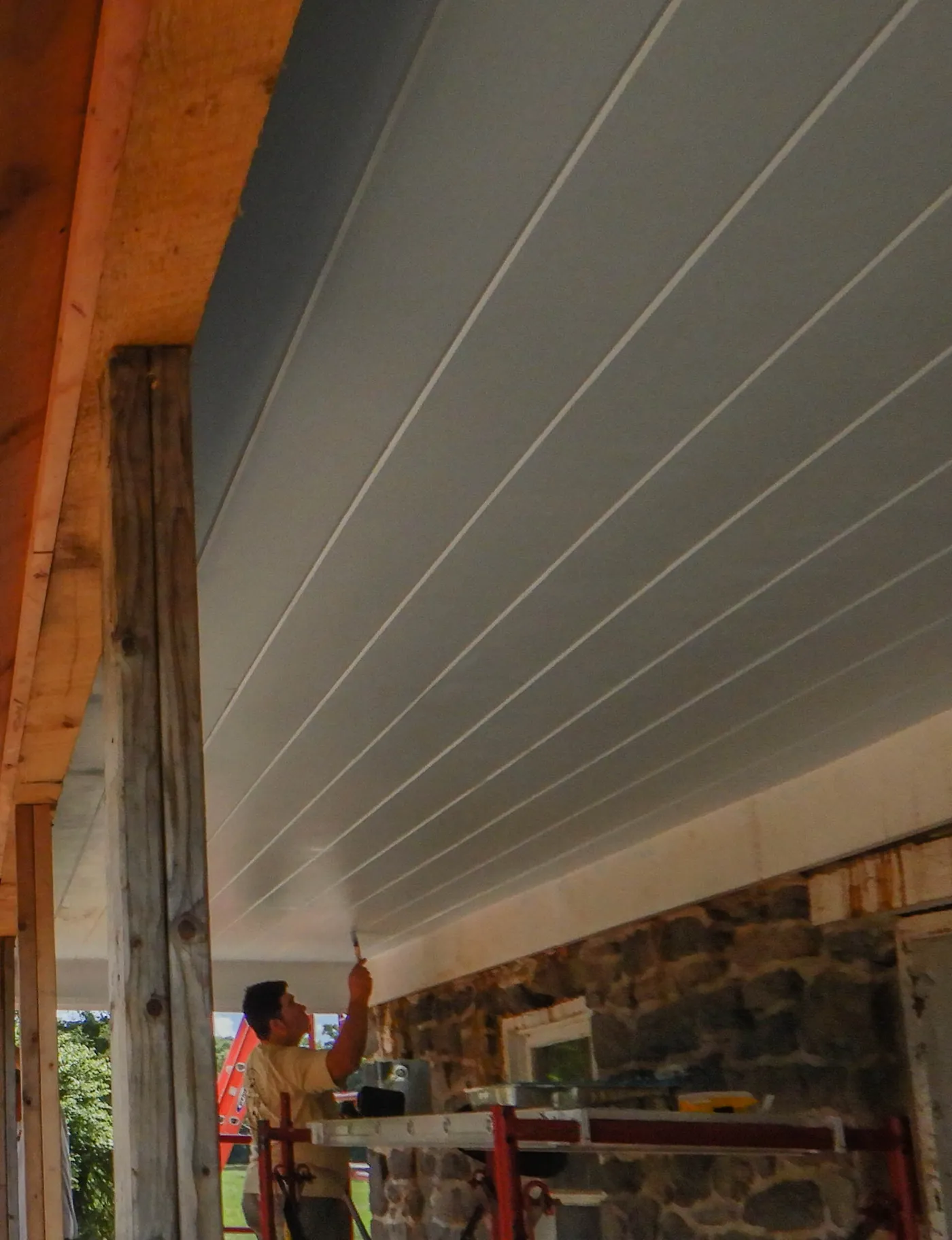 Painter brushing primer onto porch soffit boards from a scaffold