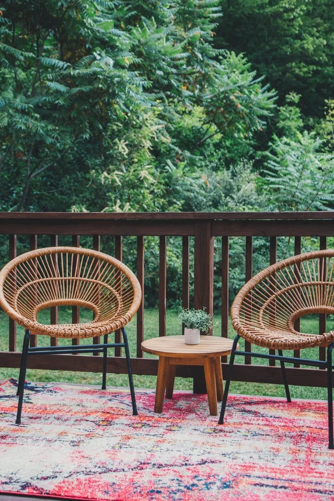 Two wicker chairs and a wooden side table on a deck by a railing